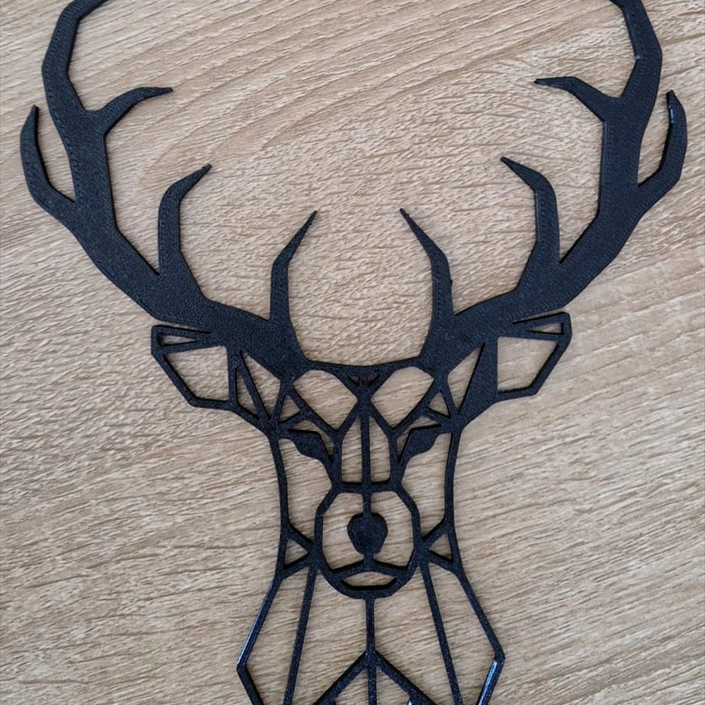 Tête de cerf géométrique imprimée en 3D, filament noir, posée sur un plan de travail en bois.